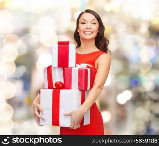 christmas, holidays, valentine&#39;s day, celebration and people concept - smiling woman in red dress with gift boxes over lights background