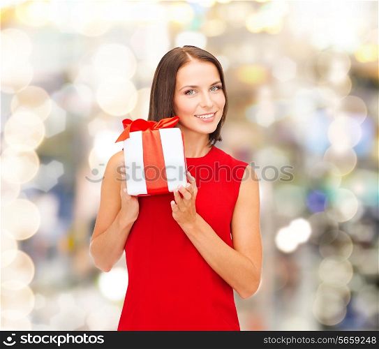 christmas, holidays, valentine&#39;s day, celebration and people concept - smiling woman in red dress with gift box over lights background