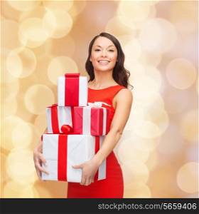 christmas, holidays, valentine&#39;s day, celebration and people concept - smiling woman in red dress with gift boxes over beige lights background