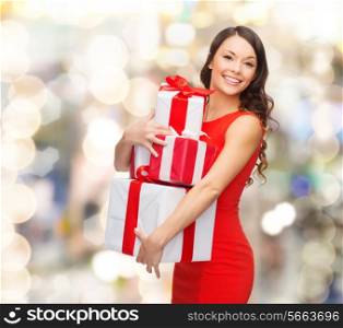 christmas, holidays, valentine&#39;s day, celebration and people concept - smiling woman in red dress with gift boxes over lights background