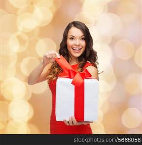 christmas, holidays, valentine&#39;s day, celebration and people concept - smiling woman in red dress with gift box over beige lights background