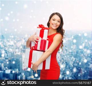 christmas, holidays, valentine&#39;s day, celebration and people concept - smiling woman in red dress with gift boxes over snowy city background