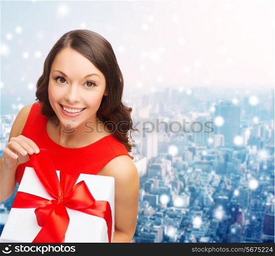 christmas, holidays, valentine&#39;s day, celebration and people concept - smiling woman in red dress with gift box over snowy city background