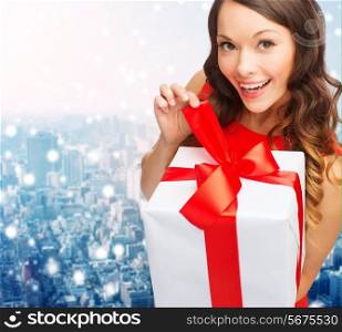 christmas, holidays, valentine&#39;s day, celebration and people concept - smiling woman in red dress with gift box over snowy city background