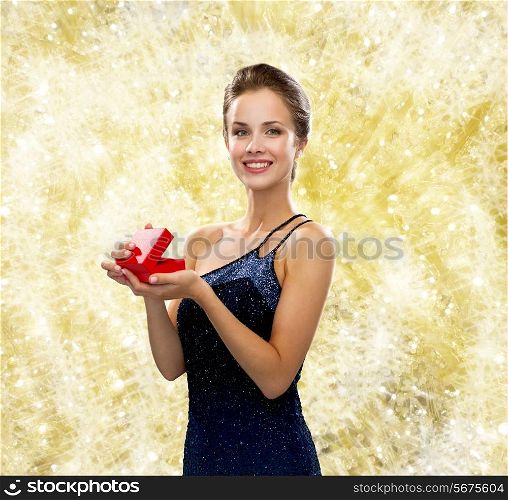 christmas, holidays, valentine&#39;s day, celebration and people concept - smiling woman in evening dress with small red gift box over yellow lights background