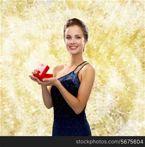 christmas, holidays, valentine&#39;s day, celebration and people concept - smiling woman in evening dress with small red gift box over yellow lights background