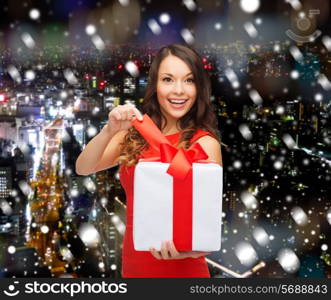 christmas, holidays, valentine&#39;s day, celebration and people concept - smiling woman in red dress with gift box over snowy night city background