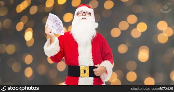 christmas, holidays, winning, currency and people concept - man in costume of santa claus with euro money over golden lights background