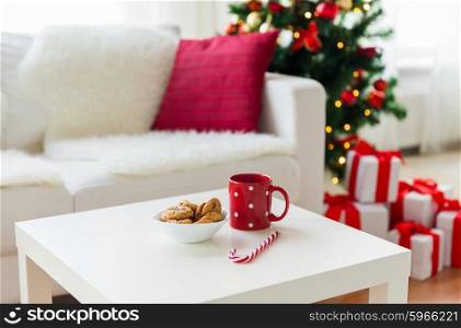 christmas, holidays, winter and celebration concept - close up of oat cookies, sugar cane candy and red cup on table at home
