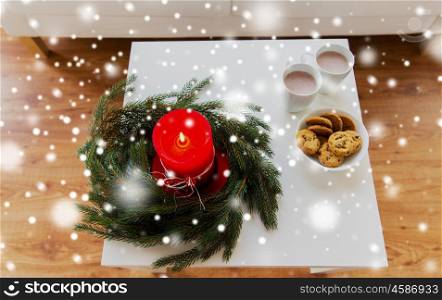 christmas, holidays, winter and still life concept - close up of fir wreath with burning candle, oat cookies and cups with hot chocolate or cocoa drink on table at home
