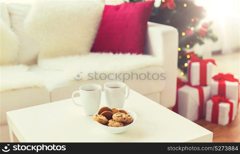 christmas, holidays, winter, celebration and still life concept - close up of cookies and cups with hot chocolate or cocoa drink on table at home. close up of christmas cookies and cups on table