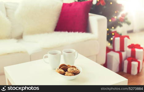 christmas, holidays, winter, celebration and still life concept - close up of cookies and cups with hot chocolate or cocoa drink on table at home. close up of christmas cookies and cups on table