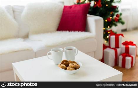 christmas, holidays, winter, celebration and still life concept - close up of cookies and cups with hot chocolate or cocoa drink on table at home