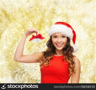 christmas, holidays, winter, happiness and people concept - smiling woman in santa helper hat with jingle bells over yellow lights background