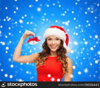 christmas, holidays, winter, happiness and people concept - smiling woman in santa helper hat with jingle bells over blue snowy background