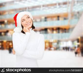 christmas, holidays, winter, happiness and people concept - thinking and smiling woman in santa helper hat over shopping center background