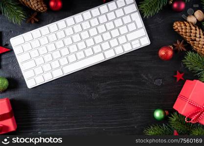 Christmas home office desk with keyboard and christmas gold decorations. Flat lay, top view, copy space over black wooden desk. Christmas home office desk