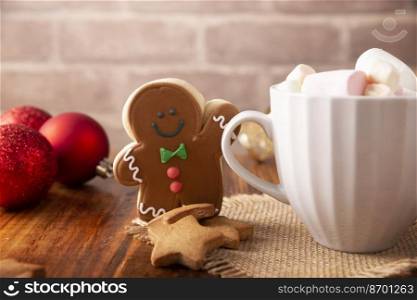 Christmas Homemade gingerbread man cookie and white cup with hot chocolate with marshmallows, traditionally made at wintertime and the holidays.