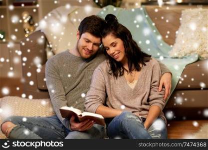 christmas, hygge and people concept - happy couple reading book at home over snow. happy couple reading book at home