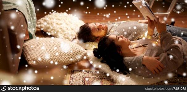 christmas, hygge and people concept - happy couple reading book at home over snow. happy couple reading book at home