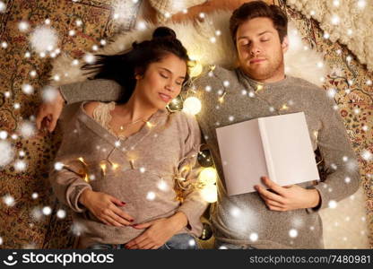 christmas, hygge and people concept - happy couple with book and garland lying on floor at home and sleeping over snow. happy couple with garland lying on floor at home