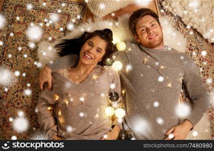 christmas, hygge and people concept - happy couple with garland lying on floor at home over snow. happy couple with garland lying on floor at home