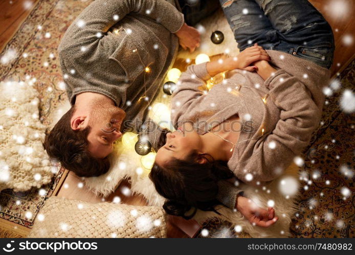 christmas, hygge and people concept - happy couple with garland lying on floor at home over snow. happy couple with garland lying on floor at home