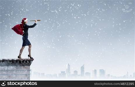 Christmas is coming. Woman in formal suit and Santa hat looking in spyglass