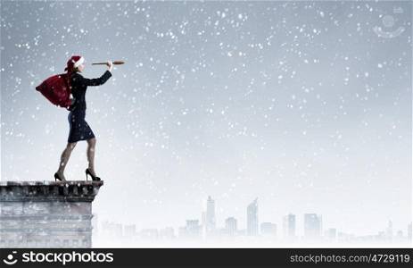 Christmas is coming. Woman in formal suit and Santa hat looking in spyglass