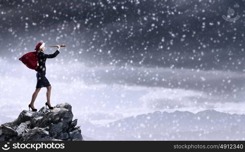 Christmas is coming. Woman in formal suit and Santa hat looking in spyglass