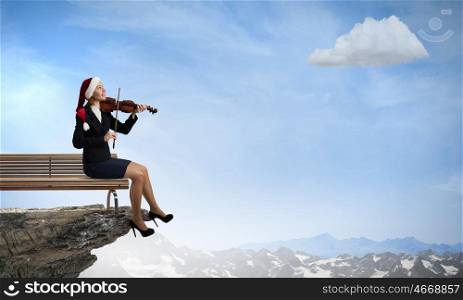 Christmas is coming. Woman in formal suit and Santa hat playing violin