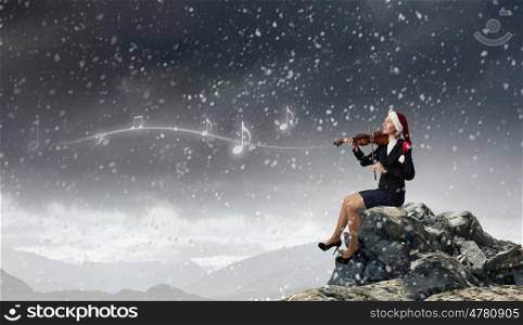 Christmas is coming. Woman in formal suit and Santa hat playing violin