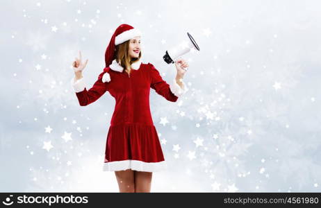 Christmas is coming. Young attractive Santa girl screaming in megaphone