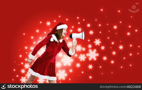 Christmas is coming. Young attractive Santa girl screaming in megaphone