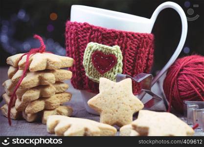 christmas - knitted woolen cups and star shaped gingerbread on a wooden table