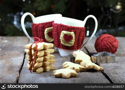 christmas - knitted woolen cups and star shaped gingerbread on a wooden table