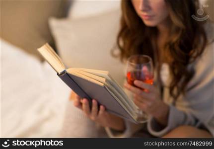 christmas, leisure and comfort concept - close up of young woman reading book and drinking rose wine from glass at home. close up of woman reading book and drinking wine