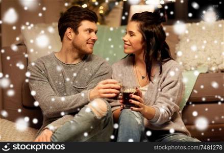 christmas, leisure and people concept - happy couple drinking coffee and eating at home over snow. happy couple drinking coffee and eating at home