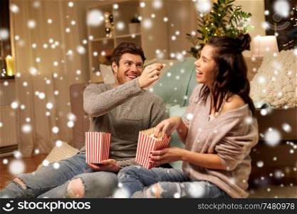 christmas, leisure and people concept - happy couple eating popcorn at home over snow. happy couple eating popcorn at home