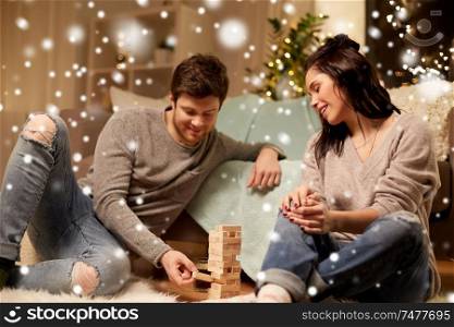 christmas, leisure and people concept - happy couple playing block-stacking game at home over snow. happy couple playing block-stacking game at home