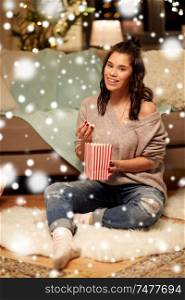 christmas, leisure and people concept - happy woman eating popcorn at home over snow. happy woman eating popcorn at home