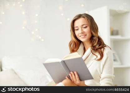 christmas, leisure and people concept - happy young woman reading book at home