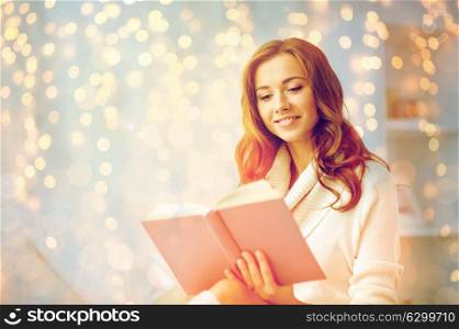 christmas, leisure and people concept - happy young woman reading book at home. happy young woman reading book at home