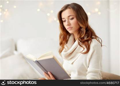 christmas, leisure and people concept - young woman reading book at home