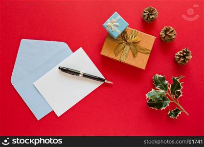 Christmas letter and pen over a red background with presents and pine cones. Christmas letter over a red background