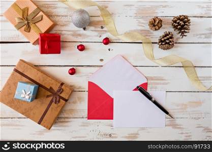 Christmas letter and pen over a rustic wooden table with presents, decorations and pine cones. Christmas letter over a rustic wooden table