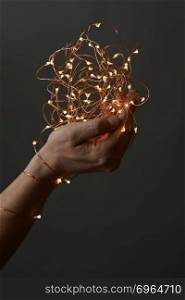 Christmas lights.Female hands holding a garland with lights on a black background. bright christmas lights in woman&rsquo;s hands