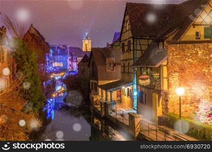 Christmas Little Venice in Colmar, Alsace, France. Traditional Alsatian half-timbered houses, church and river Lauch in Petite Venise or little Venice, old town of Colmar, decorated and illuminated at snowy christmas night, Alsace, France