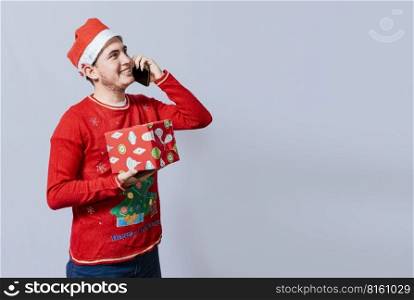 Christmas man holding gift and calling family on phone. Happy man holding gift and calling family at christmas, Smiling guy in christmas hat holding christmas gift box and talking on the phone