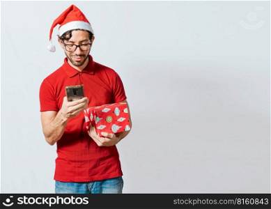 Christmas man holding gift box and telephone isolated. Handsome man in christmas hat holding gift and looking at phone, Guy in christmas hat holding gift box and smiling at smartphone